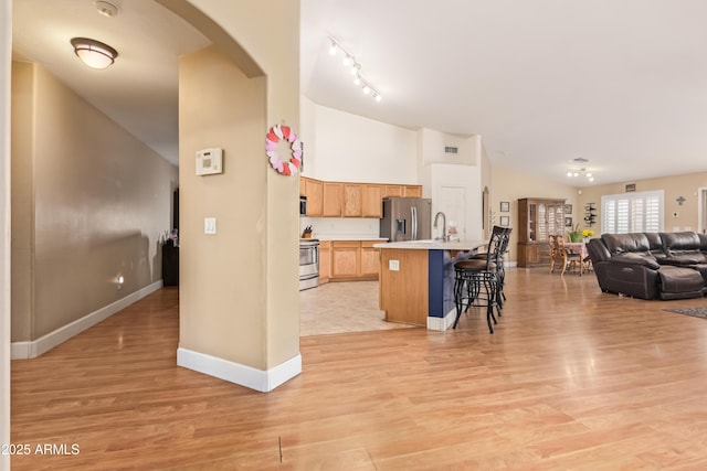 kitchen with a kitchen island with sink, light hardwood / wood-style floors, sink, appliances with stainless steel finishes, and a kitchen bar