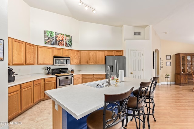 kitchen featuring appliances with stainless steel finishes, a breakfast bar, sink, high vaulted ceiling, and a kitchen island with sink