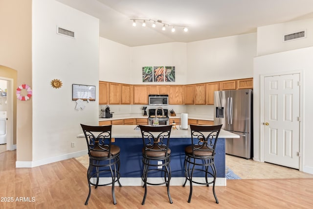 kitchen featuring a breakfast bar, a towering ceiling, stainless steel appliances, washer / clothes dryer, and a kitchen island with sink