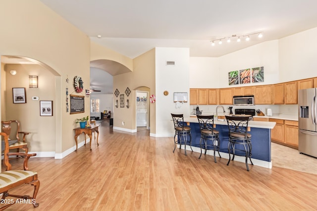 kitchen with a center island with sink, a breakfast bar, light hardwood / wood-style flooring, a high ceiling, and appliances with stainless steel finishes