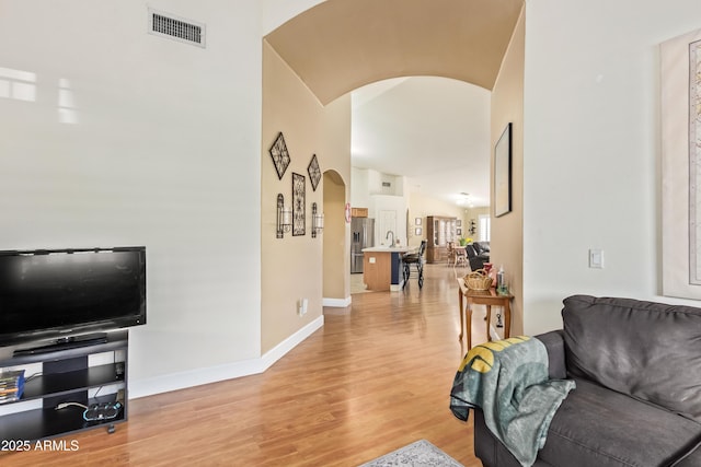 living room with sink, vaulted ceiling, and light hardwood / wood-style floors