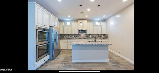 kitchen featuring tasteful backsplash, light stone countertops, appliances with stainless steel finishes, a sink, and hanging light fixtures