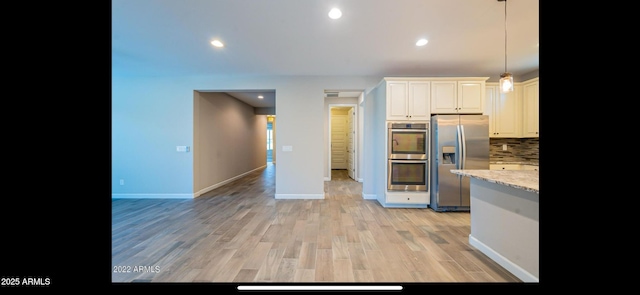 kitchen with tasteful backsplash, light wood-type flooring, appliances with stainless steel finishes, light stone counters, and baseboards