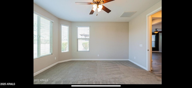 carpeted spare room with a healthy amount of sunlight, visible vents, baseboards, and ceiling fan