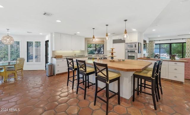 kitchen featuring built in appliances, decorative light fixtures, a center island, and white cabinets