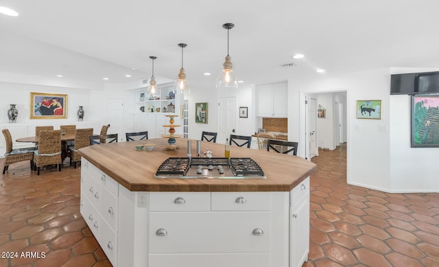 kitchen with dark tile patterned flooring, white cabinets, a center island, hanging light fixtures, and butcher block counters