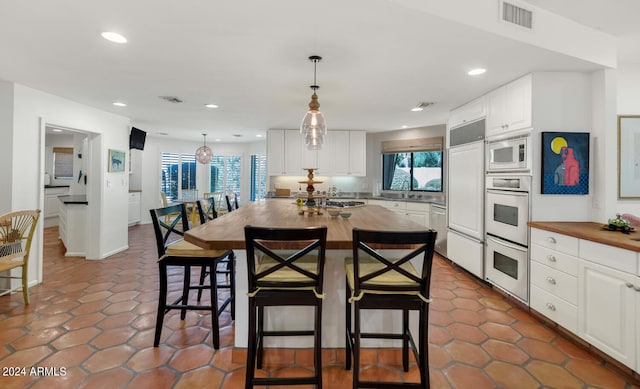 kitchen with pendant lighting, a center island, wooden counters, built in appliances, and white cabinetry