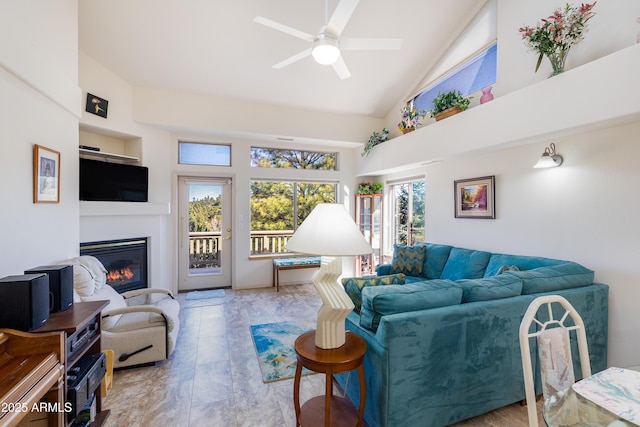 living room with high vaulted ceiling, a ceiling fan, a wealth of natural light, and a glass covered fireplace