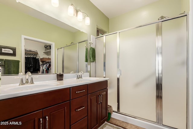 bathroom featuring a walk in closet, a shower stall, double vanity, and a sink