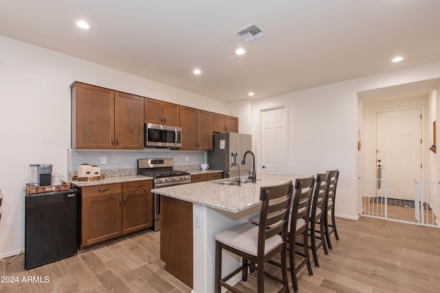 kitchen with light wood-type flooring, a kitchen bar, backsplash, and stainless steel appliances