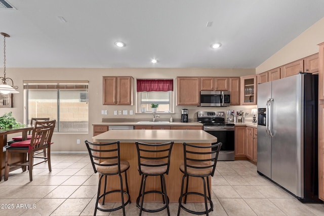 kitchen with light tile patterned floors, sink, hanging light fixtures, stainless steel appliances, and a center island