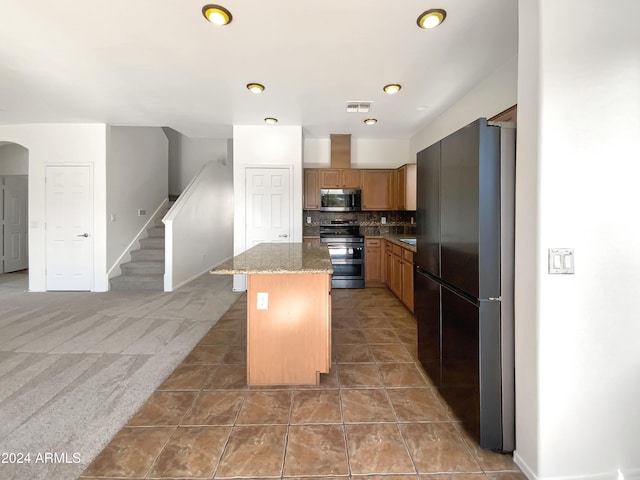 kitchen featuring light stone countertops, a kitchen island, decorative backsplash, carpet, and black appliances