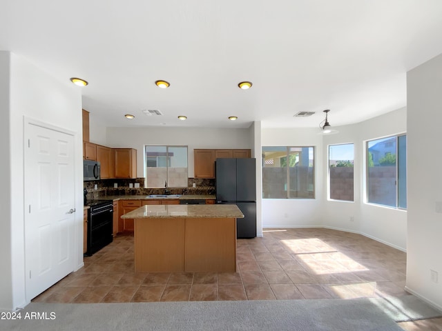 kitchen with tasteful backsplash, light stone counters, sink, black appliances, and a kitchen island