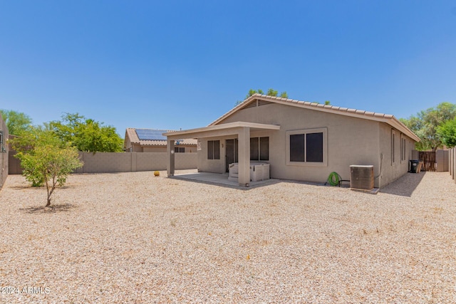 rear view of property featuring a jacuzzi, cooling unit, and a patio area