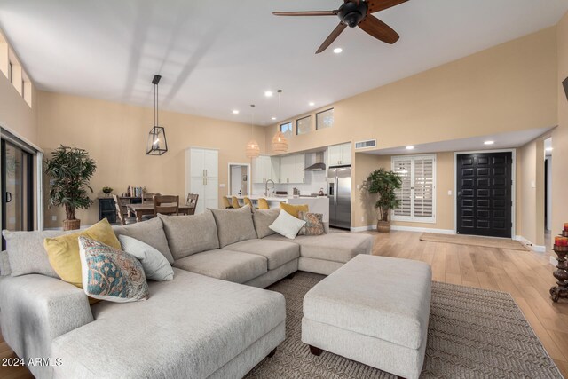 living room featuring ceiling fan, sink, light hardwood / wood-style floors, and a high ceiling