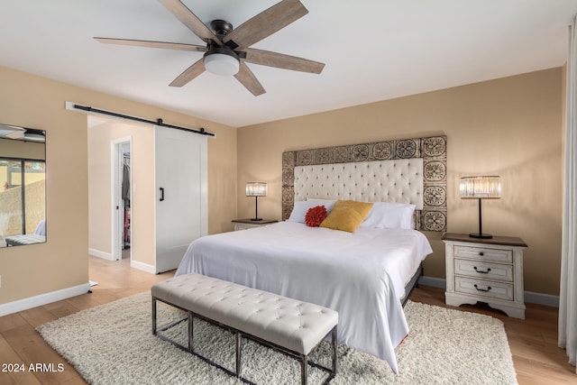 bedroom featuring ceiling fan, a spacious closet, a barn door, a closet, and light wood-type flooring