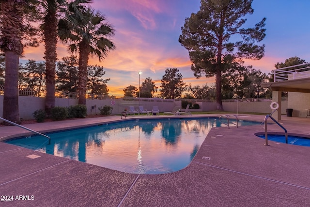 pool at dusk with a patio area and an in ground hot tub