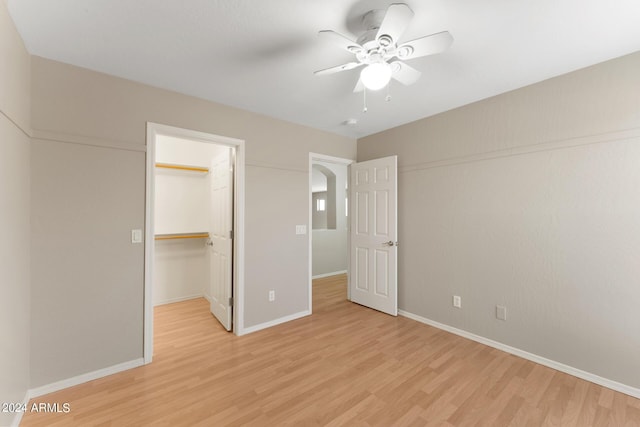 unfurnished bedroom featuring light wood-type flooring, a closet, a spacious closet, and ceiling fan