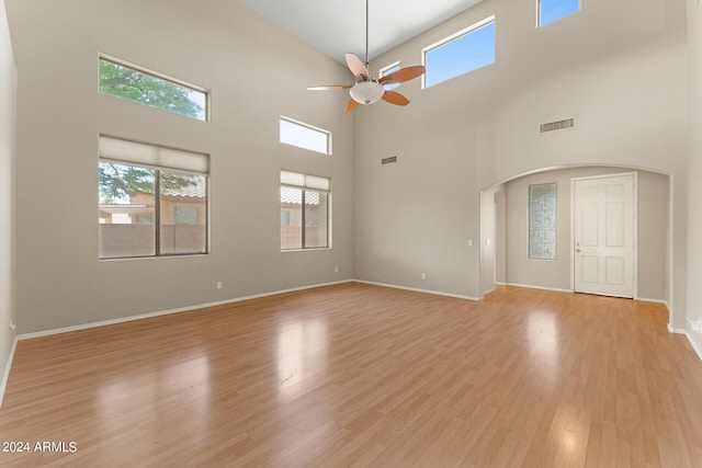 unfurnished living room featuring ceiling fan, a towering ceiling, and light wood-type flooring