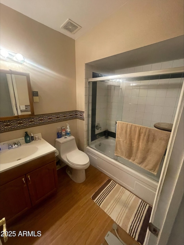 bathroom featuring visible vents, wood finished floors, vanity, toilet, and enclosed tub / shower combo