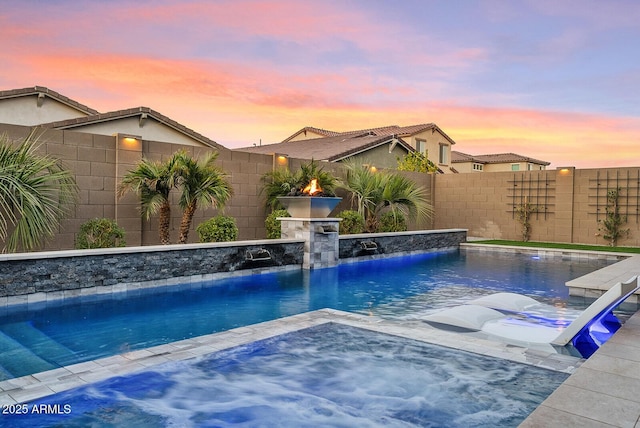 pool at dusk featuring pool water feature and a jacuzzi