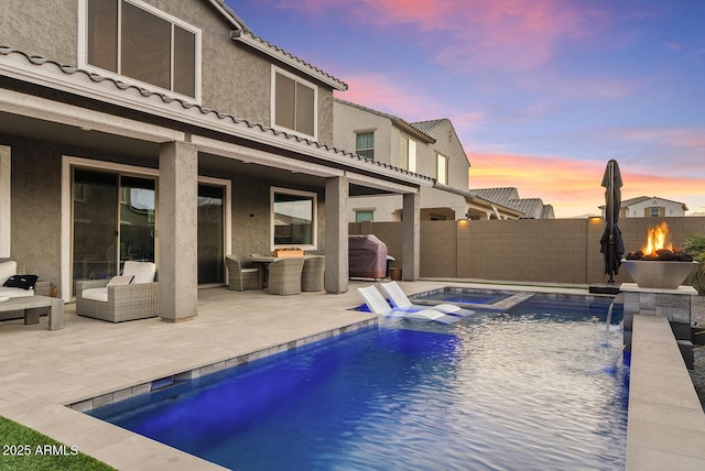 pool at dusk featuring pool water feature and a patio