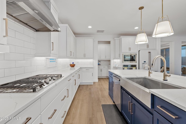 kitchen featuring blue cabinetry, white cabinets, wall chimney exhaust hood, and appliances with stainless steel finishes