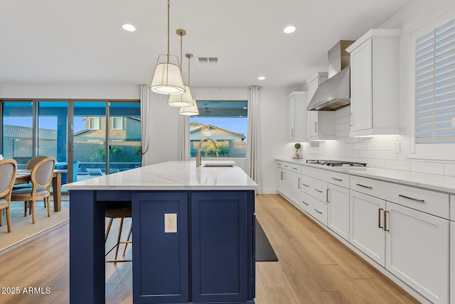 kitchen with white cabinetry, an island with sink, hanging light fixtures, and light hardwood / wood-style flooring