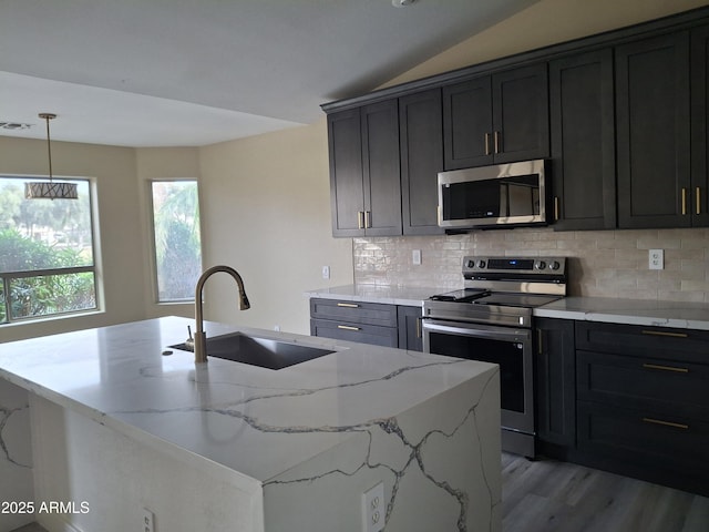 kitchen with sink, light stone counters, appliances with stainless steel finishes, a kitchen island with sink, and backsplash