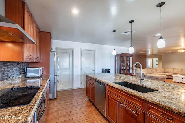 kitchen with decorative light fixtures, light stone countertops, appliances with stainless steel finishes, wall chimney range hood, and tasteful backsplash