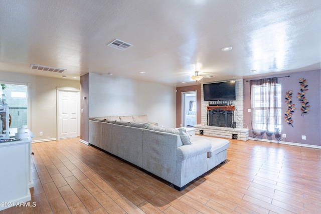 living room featuring ceiling fan, a fireplace, a textured ceiling, brick wall, and light hardwood / wood-style flooring