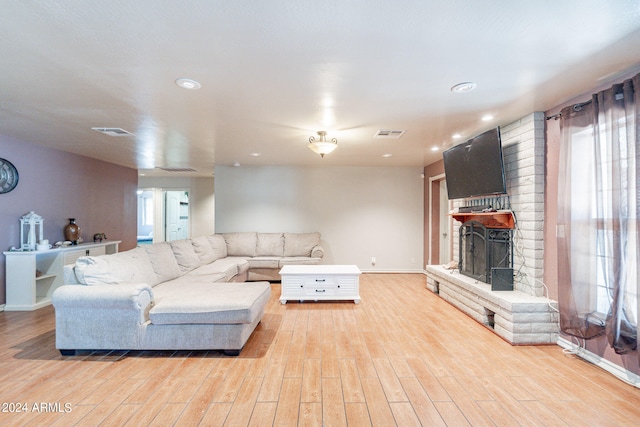 living room with light hardwood / wood-style flooring, brick wall, and a brick fireplace