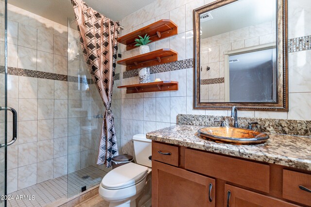 bathroom featuring tile walls, a shower with shower door, toilet, tasteful backsplash, and vanity