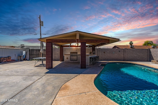 pool at dusk with exterior bar and a patio