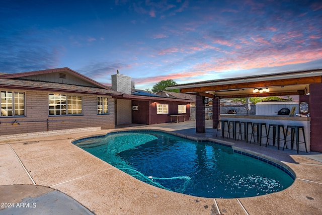 pool at dusk with a patio and an outdoor bar