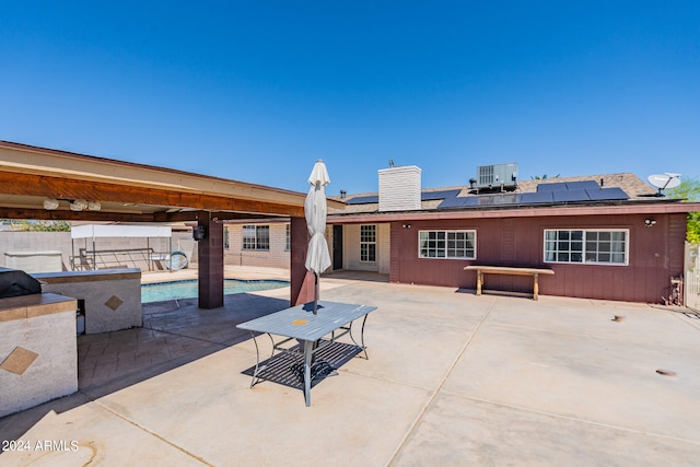 rear view of house with a patio, central AC, solar panels, and a fenced in pool