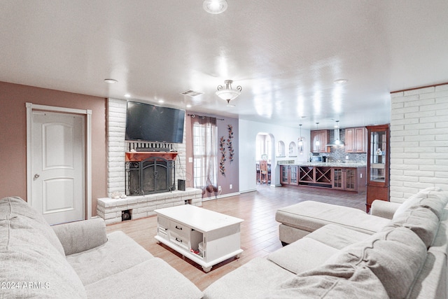 living room with brick wall, a brick fireplace, a textured ceiling, and light wood-type flooring