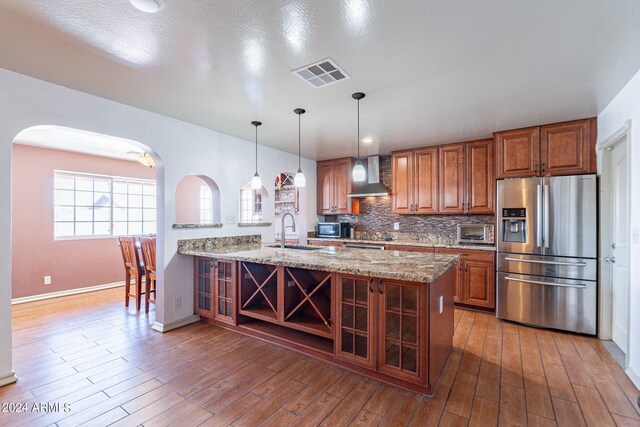 kitchen featuring stainless steel appliances, dark hardwood / wood-style floors, wall chimney range hood, light stone counters, and sink