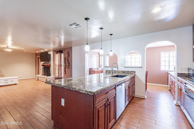 kitchen featuring hanging light fixtures, brick wall, dishwasher, dark stone counters, and sink