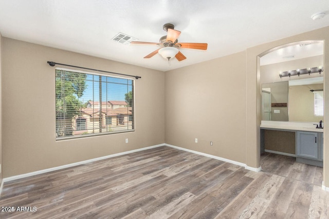 8795 W Windsor Dr, Peoria, AZ 85381 - unfurnished bedroom featuring wood finished floors, arched walkways, baseboards, connected bathroom, and ceiling fan