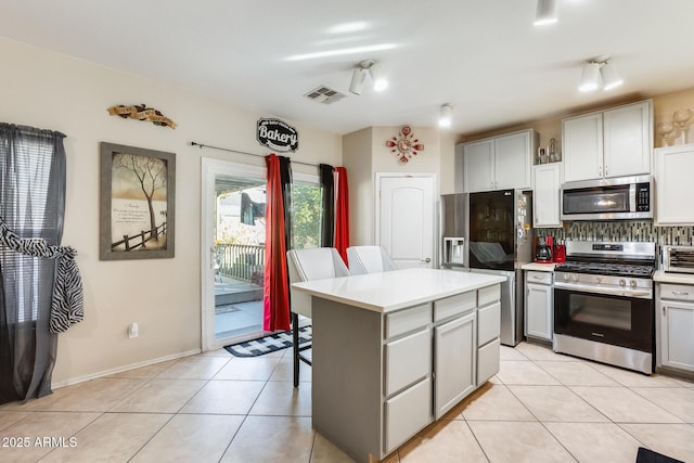 kitchen featuring a center island, appliances with stainless steel finishes, a kitchen breakfast bar, gray cabinets, and decorative backsplash