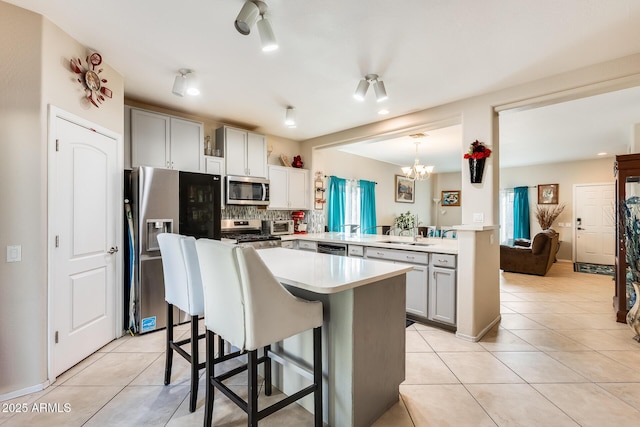 kitchen with a breakfast bar, decorative light fixtures, appliances with stainless steel finishes, kitchen peninsula, and gray cabinets