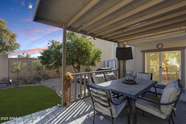 deck at dusk featuring a storage shed and a lawn