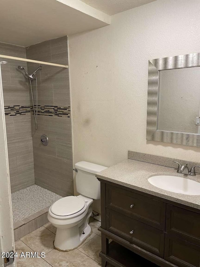 bathroom with a tile shower, tile patterned floors, vanity, and toilet