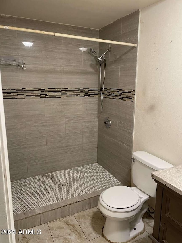 bathroom featuring tile patterned flooring, vanity, toilet, and a tile shower