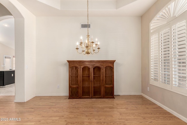 interior space featuring visible vents, arched walkways, baseboards, and light wood finished floors