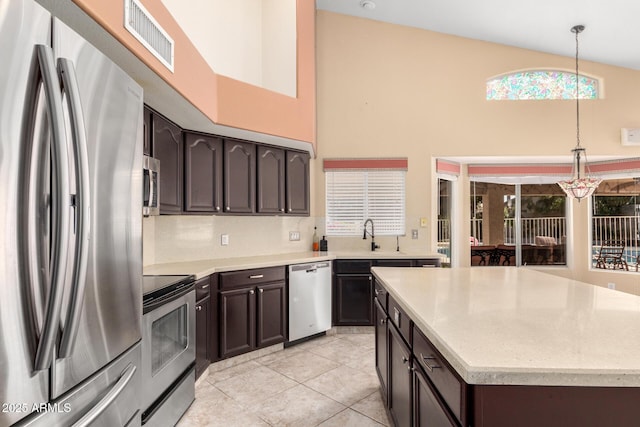 kitchen with visible vents, dark brown cabinets, appliances with stainless steel finishes, a towering ceiling, and hanging light fixtures