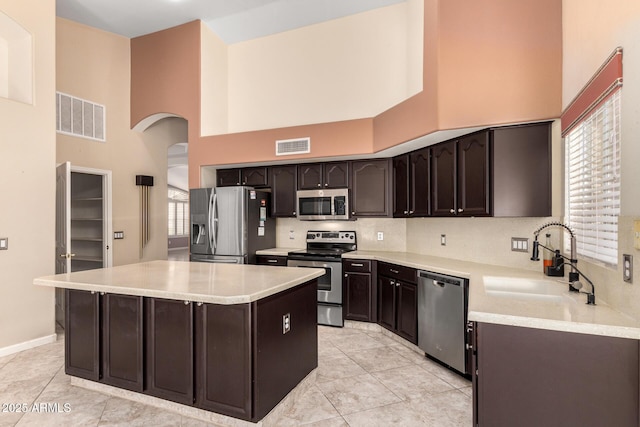 kitchen featuring visible vents, a sink, arched walkways, a high ceiling, and appliances with stainless steel finishes