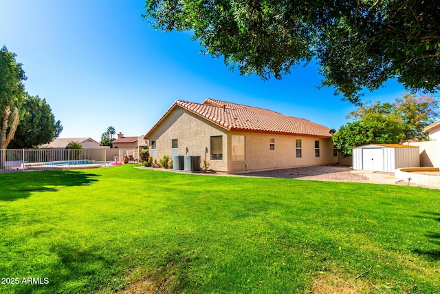 rear view of property with a shed, a tile roof, stucco siding, a yard, and a fenced backyard