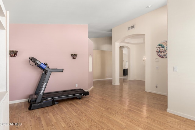 workout room with arched walkways, visible vents, light wood finished floors, and baseboards